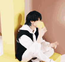 a young man with blue hair is sitting on the floor drinking from a yellow cup