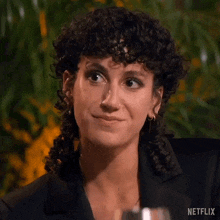 a woman with curly hair is smiling and looking at the camera while sitting at a table .