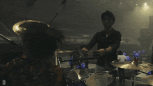 a man playing drums in a dark room with the letter d on the bottom right