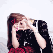 a girl making a heart shape with her hands with triangles on her face
