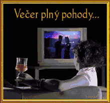 a woman is sitting on a couch holding a glass of wine and watching a tv screen with the words večer plný pohody