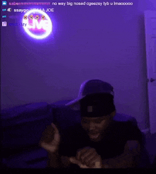 a man wearing a baseball cap is sitting in front of a purple wall with a glowing m on it .
