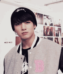 a young man wearing a black hat and a grey jacket with the letter b on the front