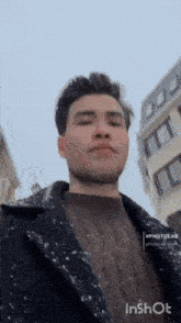 a man wearing a sweater and a coat is standing in front of a building .