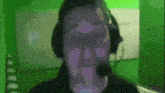 a man wearing headphones and a microphone is looking at the camera in front of a green wall .