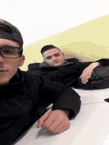 a man wearing glasses sits next to another man wearing glasses