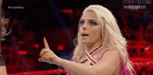 a woman in a pink dress is giving a thumbs up sign while standing in a wrestling ring .