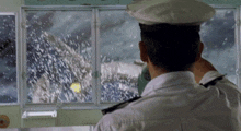 a man in a white uniform looks out a window at a snowy scene