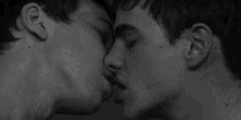 a black and white photo of two young men kissing each other .
