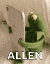 a kermit the frog is holding a cell phone and looking at it .