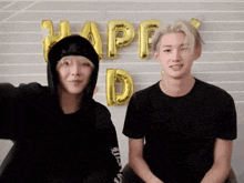 two young men sitting in front of a wall with balloons that say happy