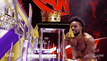 a wrestler is wearing a crown on his head while standing on a chair .