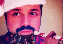 a man with a beard and a santa hat is holding a candy cane in his mouth