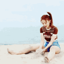 a woman wearing a striped shirt that says miu is playing in the sand on the beach