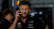 a man talking on a cell phone while wearing a red bull racing shirt