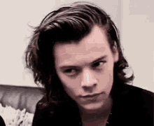 a man with long hair is sitting on a couch looking at the camera .