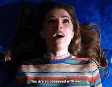 a woman in a striped sweater is laying on a blue surface and says you are so obsessed with me