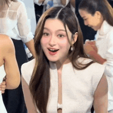 a woman in a white dress is sitting in a crowd of people and making a funny face .