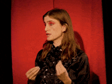 a woman with red eye shadow and a black shirt has her hands up