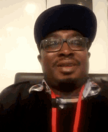 a man wearing glasses a hat and a lanyard smiles for the camera