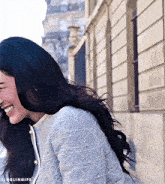 a woman with long black hair is smiling and wearing a gray jacket