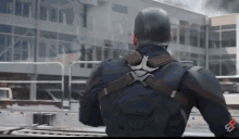 captain america is standing in front of a building with smoke coming out of the windows .