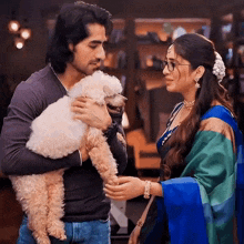 a man is holding a small white poodle while a woman looks on