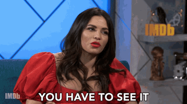 a woman in a red dress is sitting on a blue couch and says you have to see it