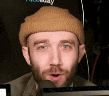 a man with a beard wearing a beanie is talking into a microphone
