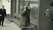 a man in a suit is talking on a cell phone while walking down the street .