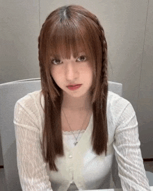 a woman with long brown hair is wearing a white shirt and a braided hairstyle .