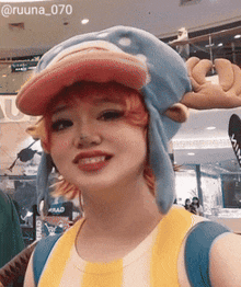 a woman wearing a blue hat with a red brim is smiling for the camera