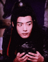 a young man with long black hair is holding a fan in his hands