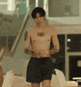 a shirtless man in black shorts has a tattoo on his arm