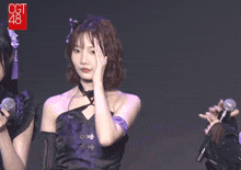 a girl in a purple dress holds her hand to her face in front of a microphone that says cgt 48