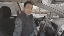 a man in a plaid shirt sits in the driver 's seat of a toyota prius