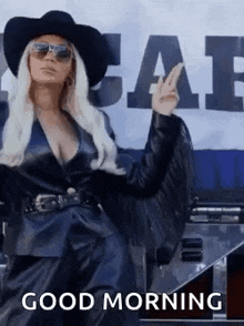 a woman wearing a cowboy hat , sunglasses and a leather jacket is giving the peace sign .