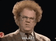 a man with curly hair and glasses is wearing a suit and tie and saying wat .