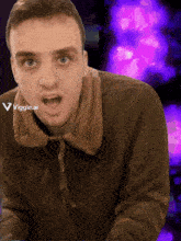a man in a brown jacket is standing in front of a purple background with the letters viggle.ai visible