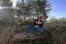 a man wearing sunglasses and a red hat is squatting down in a grassy field