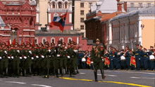 a group of soldiers marching in a parade with a flag in the background