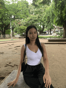 a woman in a white tank top sits on a bench