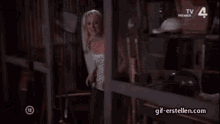 a woman in a white dress is opening a box in a warehouse with tv premier on the bottom right