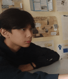 a young boy sits at a desk in front of a wall with papers on it including one that says " representations "