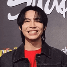 a young man wearing a red shirt and a black jacket smiles