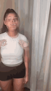 a woman in a white shirt and black shorts is standing in front of a curtain .