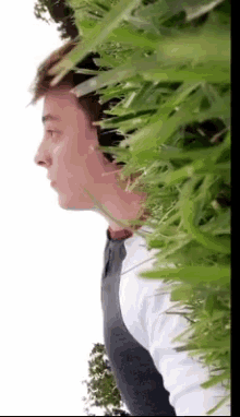 a man in a white shirt stands in front of a bush