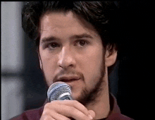 a man with a beard is holding a microphone in front of his mouth .