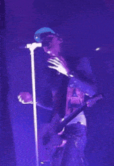 a man in a blue hat is singing into a microphone while holding a guitar
