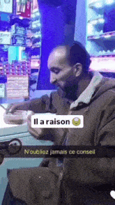 a man is sitting at a table with a sign that says ' il a raison ' on it